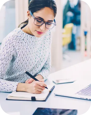 Woman wearing glasses writing notes at office desk